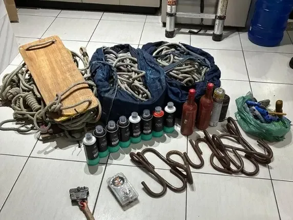 Homem algemado, com expressão séria, sendo conduzido por policiais em delegacia.