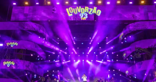 Multidão de fiéis com mãos levantadas em adoração no festival gospel Louvorzão 93, no Rio de Janeiro, com palco iluminado e b