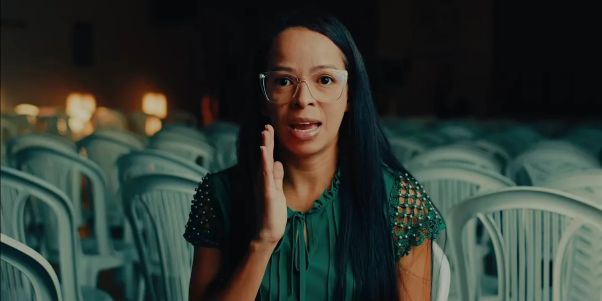 Pastora Jany Lima, ex-líder de gangue, prega no púlpito com Bíblia aberta, olhando confiante para a câmera.