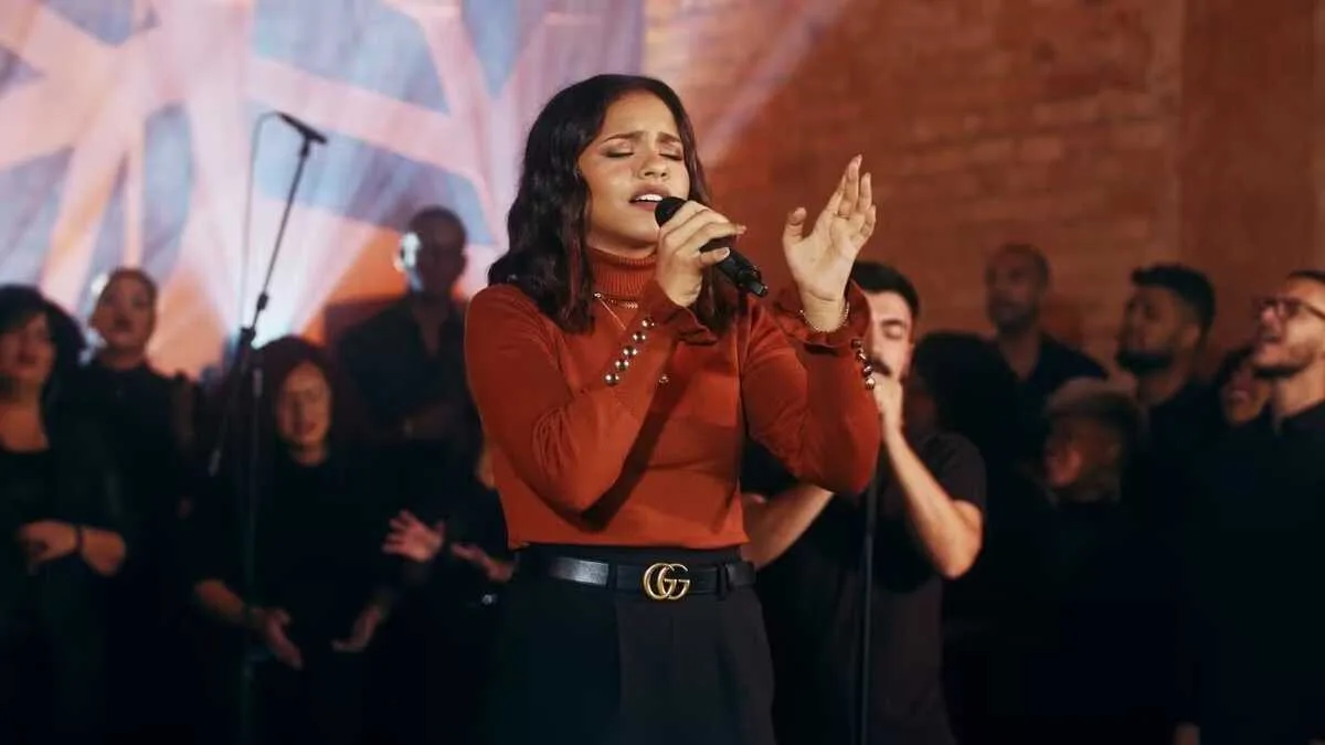 Julia Vitória sorri segurando discos de Platina e Diamante no palco da IPALPHA Campus Tamboré, em São Paulo, com plateia ao f