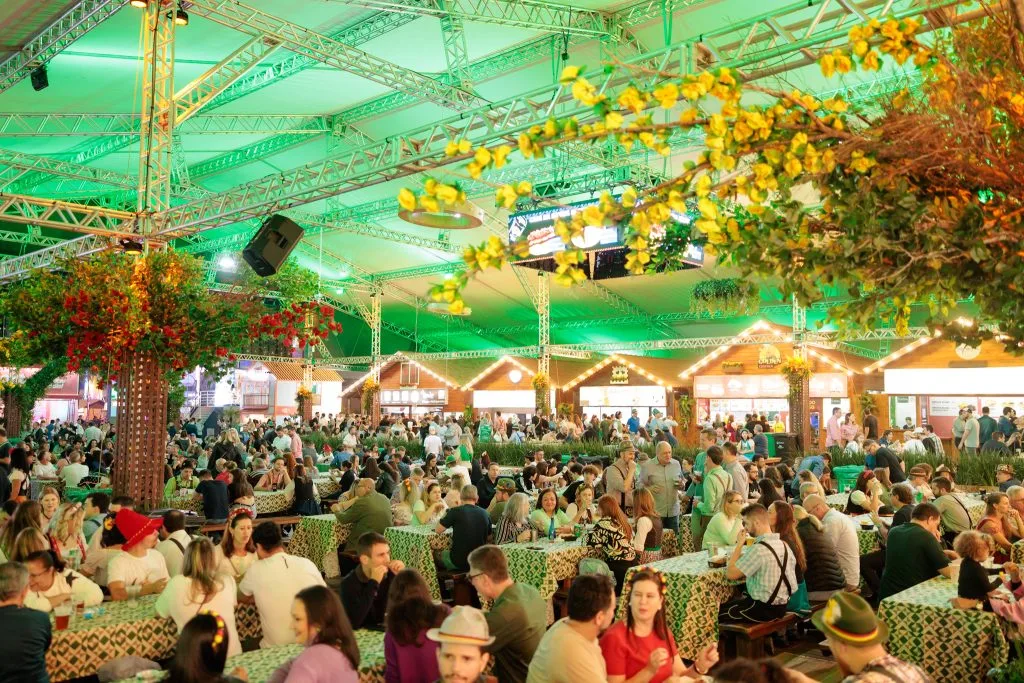 Várias pessoas distribuídas em mesas no centro de uma praça de alimentação da Oktoberfest Blumenau